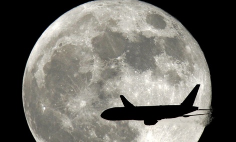 A jet plane passes in front of the full moon. 