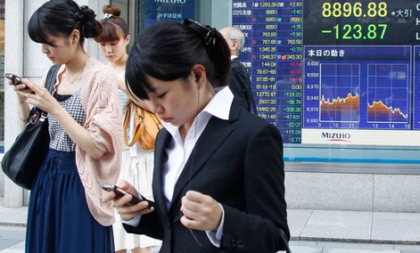 Japanese women operate mobile phones in front of the stock index display of a securities firm in Tokyo. Japanese women operate mobile phones in front of the stock index display of a securities firm in Tokyo.