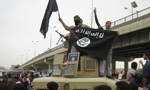 Islamic State group militants hold up their flag as they patrol in a commandeered Iraqi military vehicle in Fallujah.