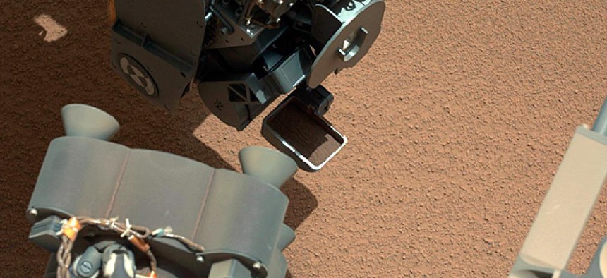 The Curiosity Rover uses it's robotic arm to scoop sand.