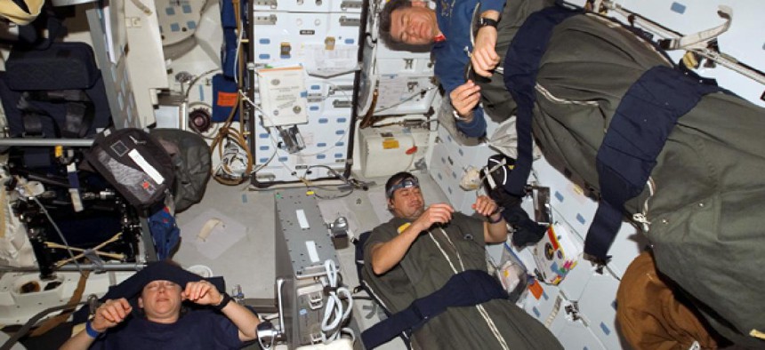 Astronauts Pam Melroy, George Zamka, bottom right,and European Space Agency's Paolo Nespoli, sleep in their sleeping bags, which are secured on the middeck of the Space Shuttle Discovery while docked with the International Space Station.