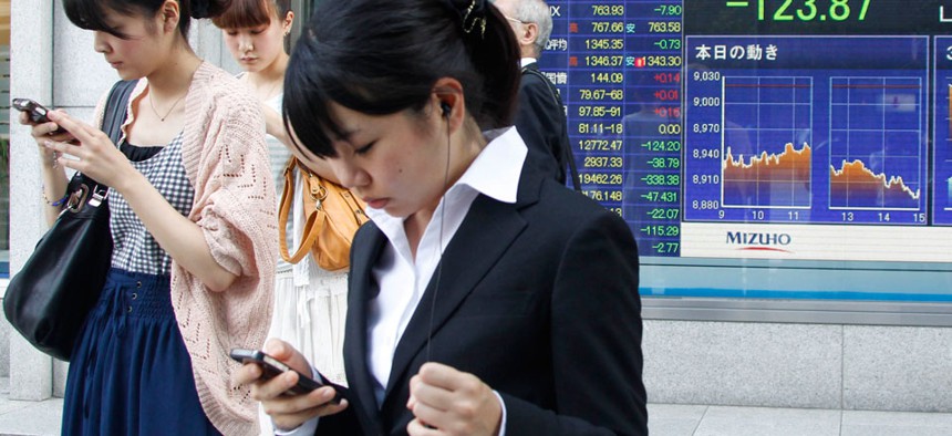 Japanese women operate mobile phones in front of the stock index display of a securities firm in Tokyo.