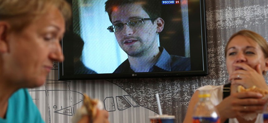 Two Russians eat lunch at Moscow's Sheremetyevo airport while a report about Edward Snowden plays on a nearby TV.