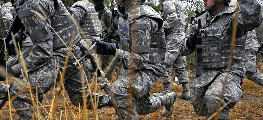 Air Force basic trainees in body armor use hand signals as they take a knee during a tactical drill movement.
