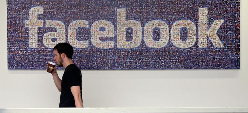 A Facebook employee walks past a sign at Facebook headquarters in Menlo Park, Calif.