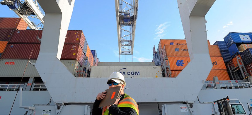A dock worker communicates on a walkie-talkie while a ship to shore crane loads containers onto a ship at the Georgia Ports Authority Garden City terminal.