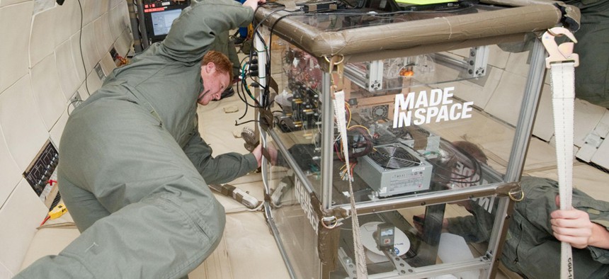 Two people monitoring the performance of extruders inside the Made In Space experiment box during a microgravity portion of flight aboard a modified Boeing 727 from the Zero G Corporation.