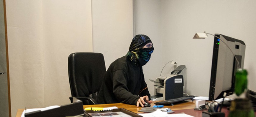 A masked pro-Russian activist sits in front of a computer inside a room.