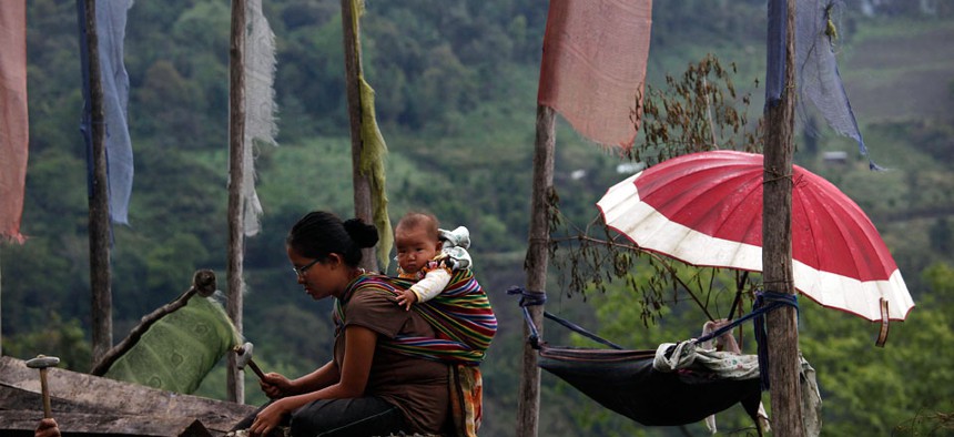 A Bhutanese woman carries her baby on her back as she works on a mountain roadside.