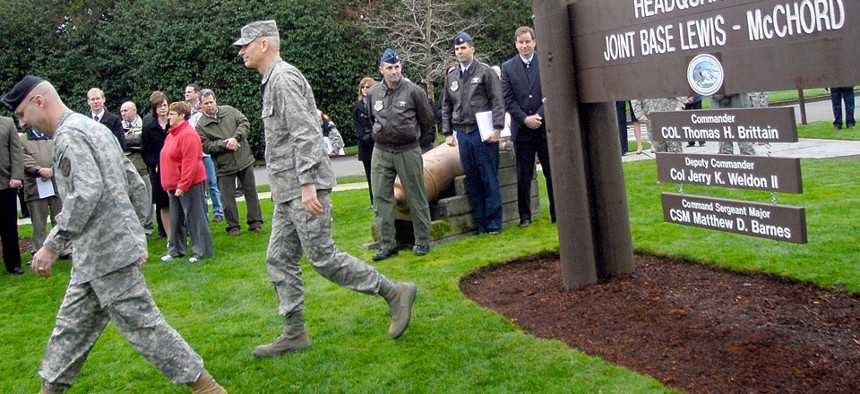 Army Col. Thomas Brittain, left, and Air Force Col. Kenny Weldon walk away from the new headquarters sign after a ceremony marking attainment of initial operational capability for Joint Base Lewis-McChord.