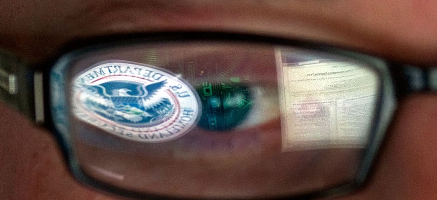 A reflection of the Department of Homeland Security logo is seen reflected in the glasses of a cyber security analyst at DHS.
