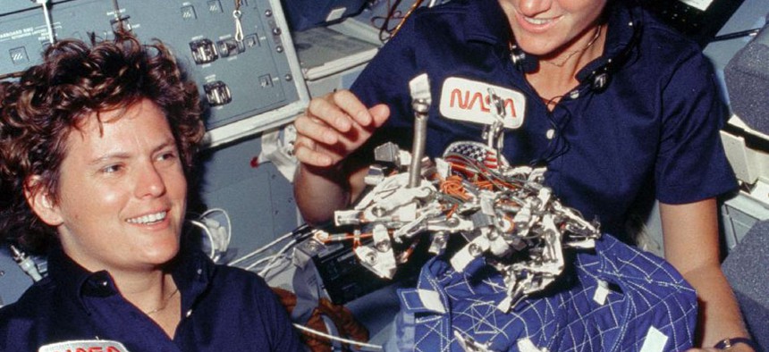 Astronauts Kathryn D. Sullivan, left, and Sally K. Ride display a "bag of worms" during the STS-41G mission in 1984. The bag is a sleep restraint and the majority of the 'worms' are mostly springs and clips used with the sleep restraint. 