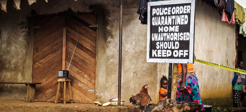 A child, center, stands underneath a signboard reading 'Police order quarantined home unauthorised should keep off' as a family home is placed under quarantine due to the Ebola virus in Port Loko, Sierra Leone.