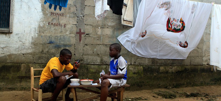 Mohammed Kromah, left, 26, and his half-brother Michell Pratt listen to election results on the radio of a cell phone while eating lunch outside their house in the Sinkor neighborhood of Monrovia, Liberia.