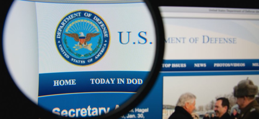 Photo of the United States Department of Defense homepage on a monitor screen through a magnifying glass.
