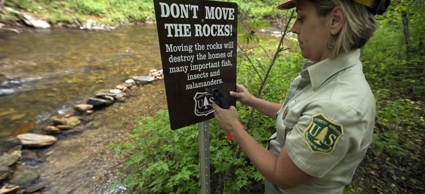 The work of the US Forest Service: Pisgah National Forest Forest Service biologist Lorie Stroup installs a sign to remind forest users about the sensitivity of streambed habitats. 