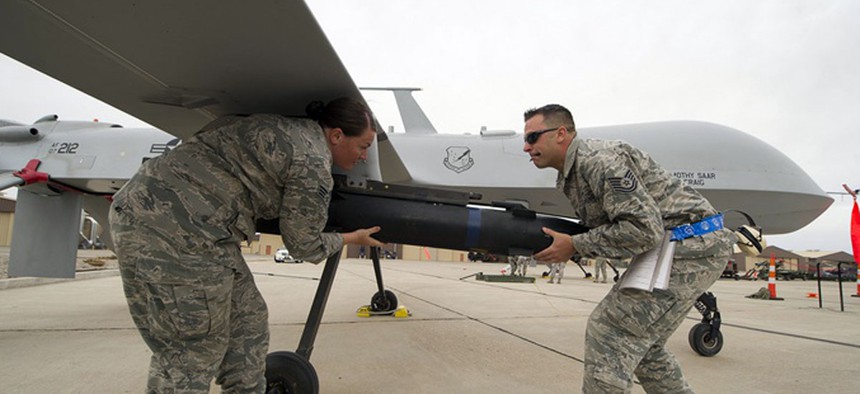 Two Air Force NCOs load munitions on an MQ-9 Predator.