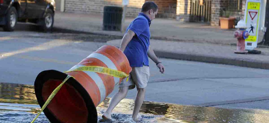 Harris Carter, owner of Castaways & Grill in the historic section of Georgetown, moves a road barrier to block traffic as high tide approaches historic downtown Georgetown, S.C., Thursday, Oct. 8, 2015.