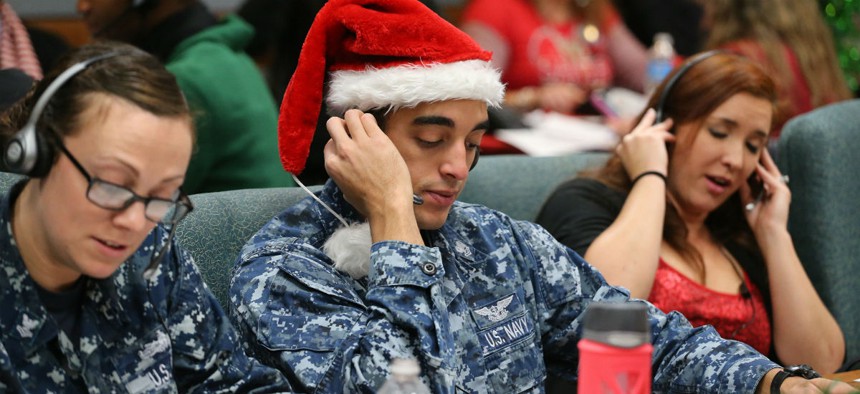 Santa tracker volunteers U.S. Navy Petty Officer Brandon Wright, center, and his wife, Petty Officer Emily Wright, left, take phone calls from children asking where Santa is and when he will deliver presents to their homes, inside a phone-in center during
