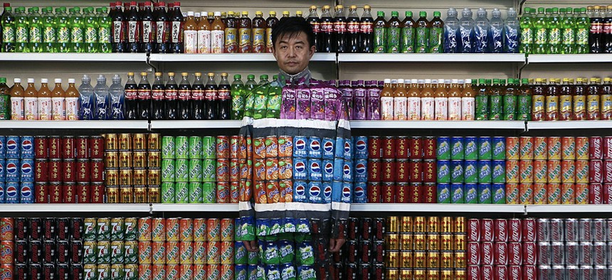 Chinese artist Liu Bolin waits for his colleagues to put a finishing touch on him to blend into rows of soft drinks in his artwork entitled "Plasticizer".