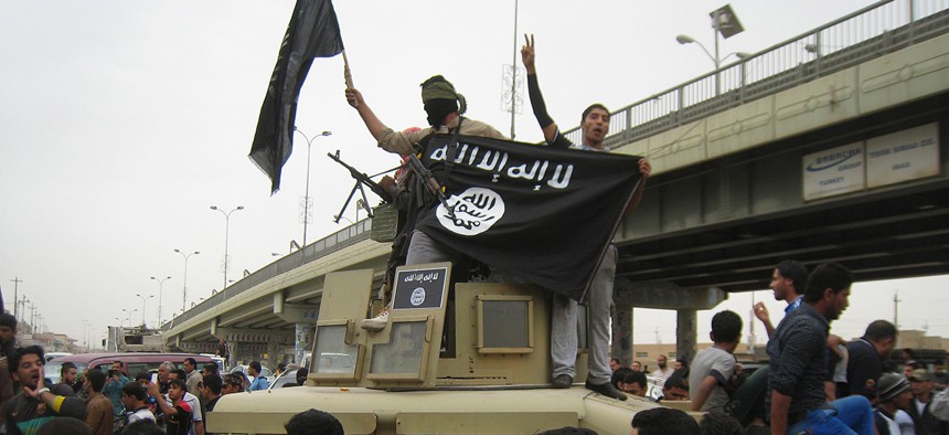 Islamic State group militants hold up their flag as they patrol in a commandeered Iraqi military vehicle in Fallujah.