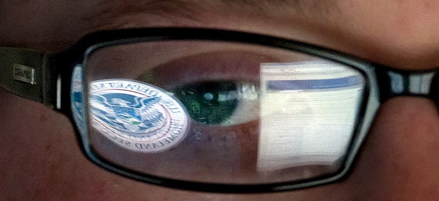 A reflection of the Department of Homeland Security logo in the eyeglasses of a cybersecurity analyst.