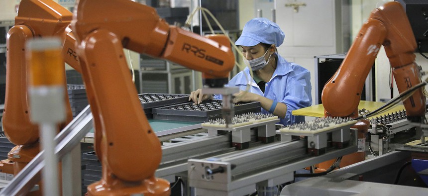 A Chinese woman works amid orange robot arms at Rapoo Technology factory in southern Chinese industrial boomtown of Shenzhen. 