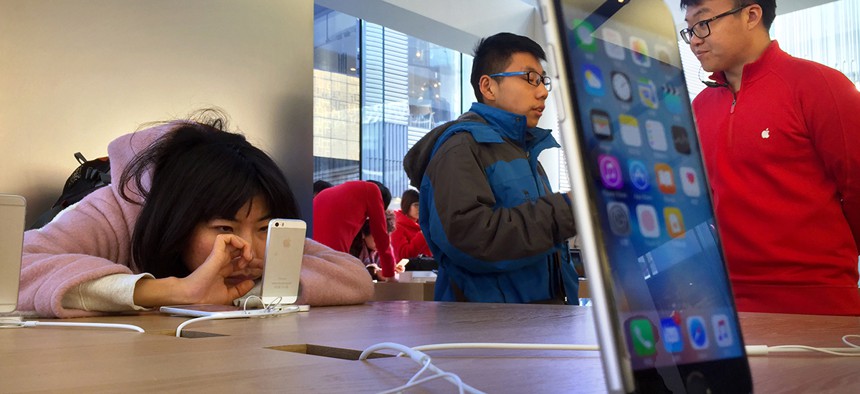 A woman uses a displayed iPhone as a customer talks with an employee, right, at an Apple Store in Beijing, Thursday, Feb. 18, 2016.