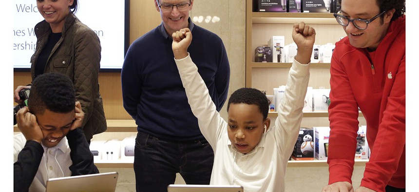 Third-grader Jaysean Erby raises his hands as he solves a coding problem as Apple CEO Tim Cook watches from behind during a coding workshop at an Apple Store, in New York.