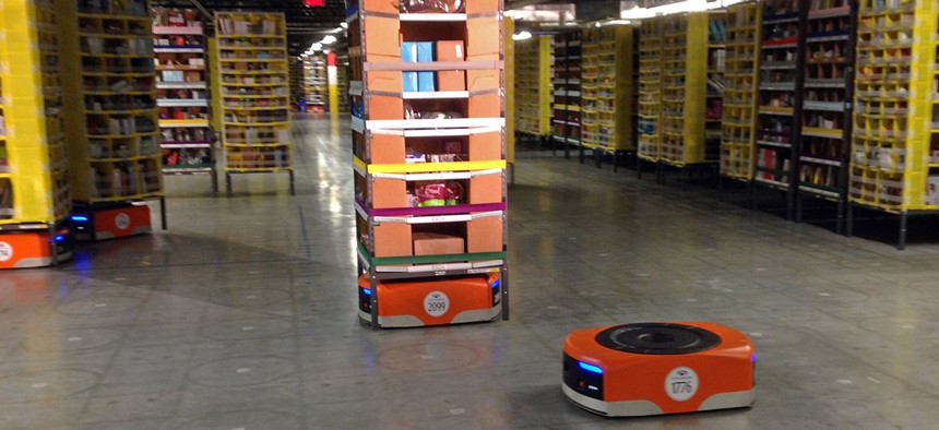 A Kiva robot drive unit is seen, foreground, before it moves under a stack of merchandise pods, seen on a tour of one of Amazon's newest distribution centers in Tracy, Calif.
