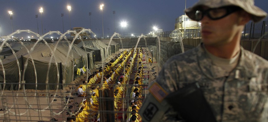 A U.S. soldier stands guard as detainees pray at U.S. military detention facility Camp Bucca, Iraq.