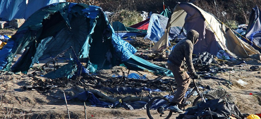 A migrant rides with his bicycle in the Calais refugee camp, northern France Tuesday, Jan. 19, 2016.