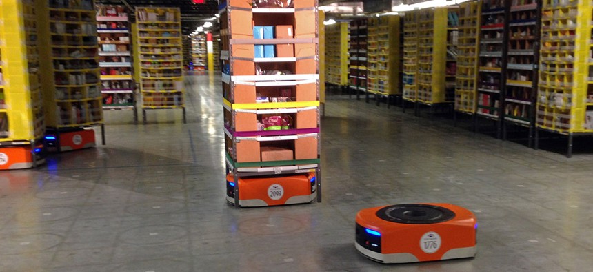 A Kiva robot drive unit is seen, foreground, before it moves under a stack of merchandise pods, seen on a tour of one of Amazon's newest distribution centers in Tracy, Calif.