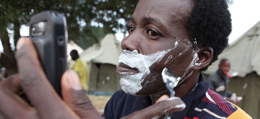 A man shaves himself, using his mobile phone as a mirror at a temporary shelter set up for foreign nationals fleeing attacks from South Africans in and around Johannesburg Sunday, April 19, 2015. 