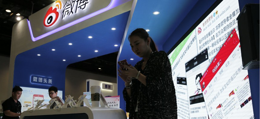A woman browses her smartphone near a display booth for China's Weibo microblogging website at the 2016 Global Mobile Internet Conference in Beijing, April 28, 2016.