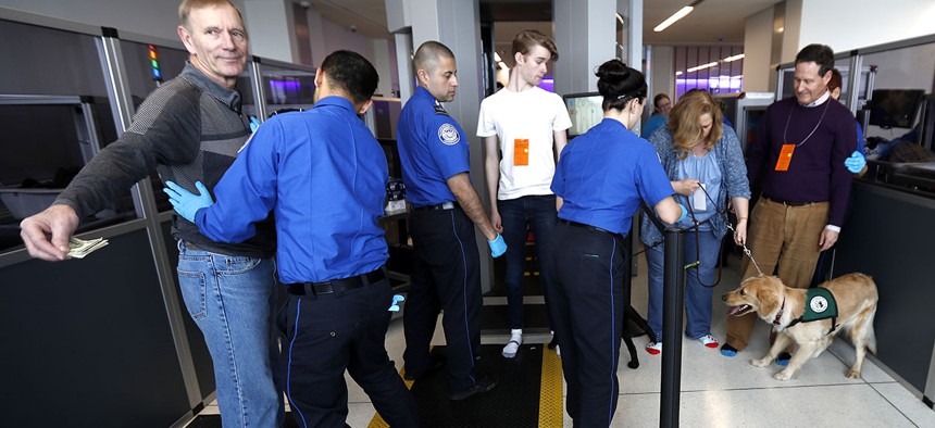 A traveler, left, is padded by a TSA agent as trainers, top right, lead their service dogs through the security area at Newark Liberty International Airport while taking part of a training exercise, Saturday, April 1, 2017