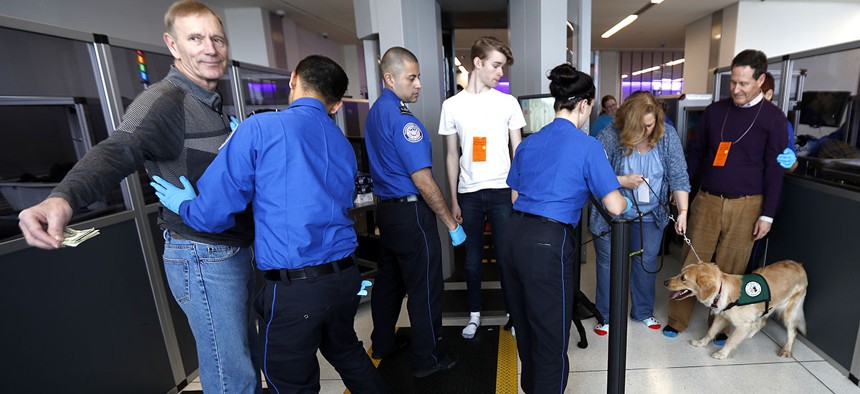 A traveler, left, is padded by a TSA agent as trainers, top right, lead their service dogs through the security area at Newark Liberty International Airport while taking part of a training exercise, Saturday, April 1, 2017.