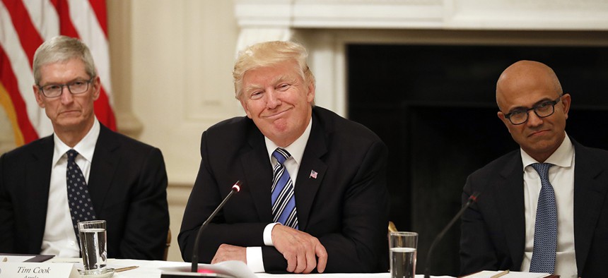 President Donald Trump, center, smiles as he is seated between Tim Cook, Chief Executive Officer of Apple, left, and Satya Nadella, Chief Executive Officer of Microsoft, right, during an American Technology Council roundtable.
