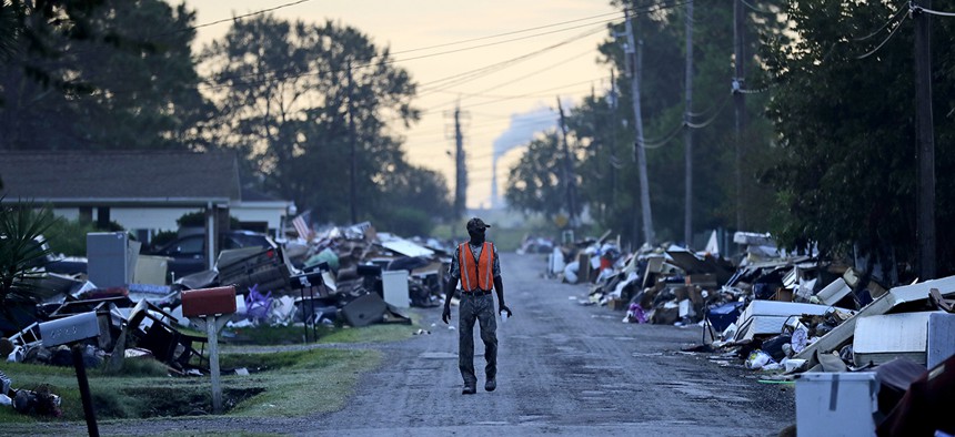 A man walks past debris from homes on his street damaged in flooding from Hurricane Harvey as an oil refinery stands in the background in Port Arthur, Texas, Thursday, Sept. 28, 2017. 