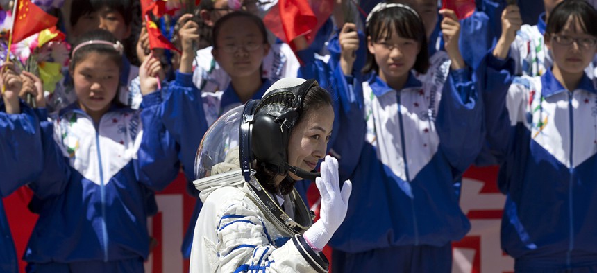 Chinese students wave flowers and national flags as female astronaut Wang Yaping leaves the Jiuquan satellite launch center for the launch site, near Jiuquan in western China's Gansu province, Tuesday, June 11, 2013.