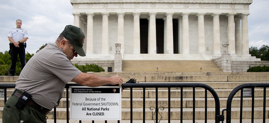 A U.S. Park Police officer watches at left as a National Park Service employee posts a sign on a barricade closing access to the Lincoln Memorial in Washington. 
