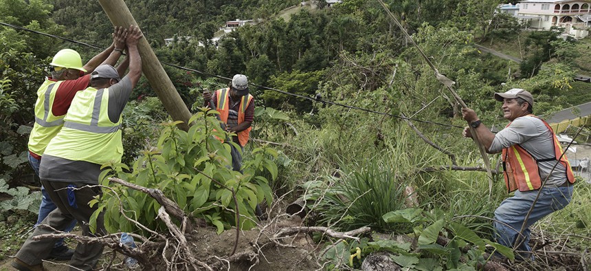Public Works Sub-Director Ramon Mendez, wearing a hard hat at left, works with locals who are municipal workers, from right, Eliezer Nazario, Tomas Martinez and Angel Diaz as they install a new post to return electricity in Coamo, Puerto Rico.
