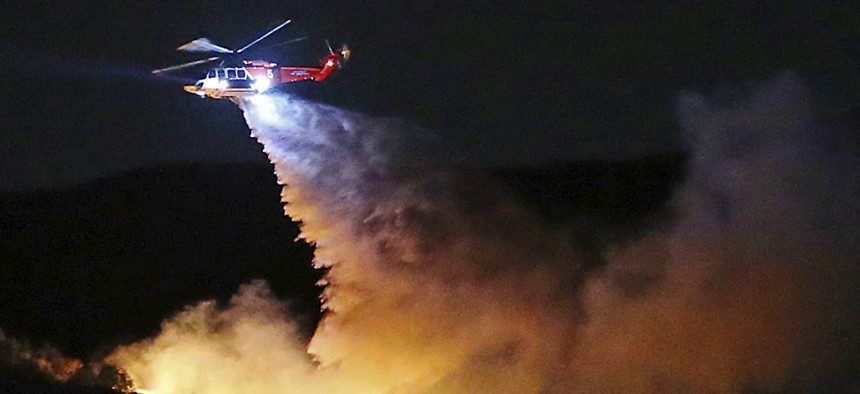 a helicopter drops water on a brush fire that broke out in Topanga State Park, Los Angeles. 