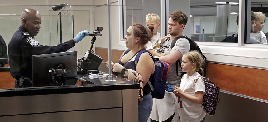 A customs agent, left, adjusts a face recognition camera as he screens a family after their recent international flight arrival at Orlando International Airport, Thursday, June 21, 2018.