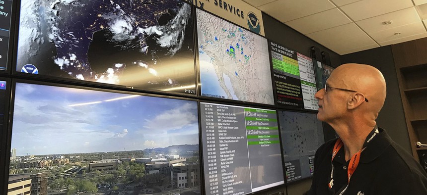 In this Wednesday, July 18, 2018 photo, National Weather Service forecaster Marvin Percha reviews monitors that track satellite and Doppler radar images, as well as his colleagues' forecasts posted on social media, at the agency's operating center in Az.
