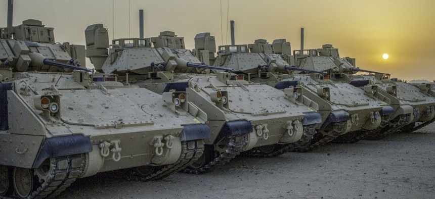 Four M2A3 Bradley Infantry Fighting Vehicles are illuminated by the rising sun in a motor pool located at Camp Buehring, Kuwait, July 19, 2018.