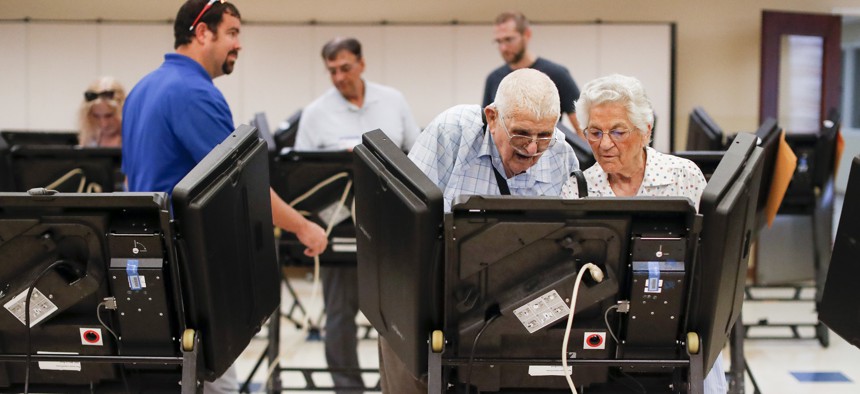 Voters cast their ballots among an array of electronic voting machines in a polling station.