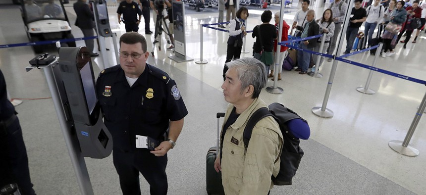 U.S. Customs and Border Protection supervisor Erik Gordon, left, helps a passenger navigate one of the new facial recognition kiosks at a United Airlines gate before boarding a flight to Tokyo.