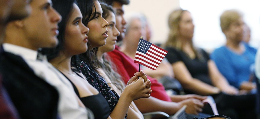 New citizens hold an American flag as they listen during a naturalization ceremony at the U.S. Citizenship and Immigration Services Kendall Field Office, Thursday, Aug. 30, 2018, in Miami.