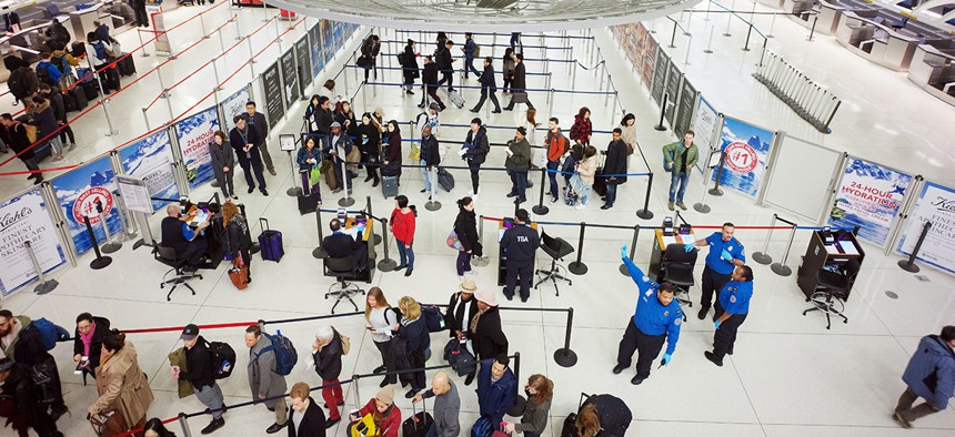 passengers stand in line as they wait to pass through a TSA security checkpoint at JFK International Airport.